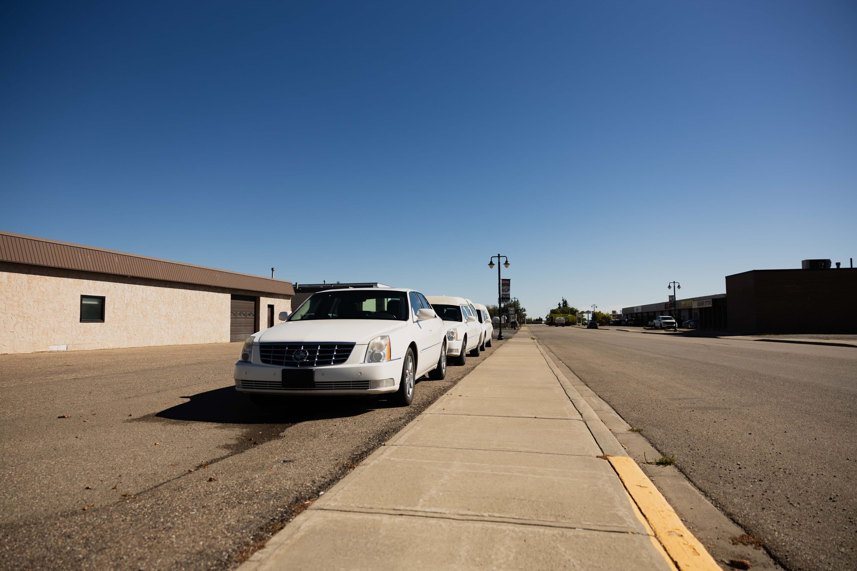 White hearses parked outside a small-town funeral home under a clear blue sky