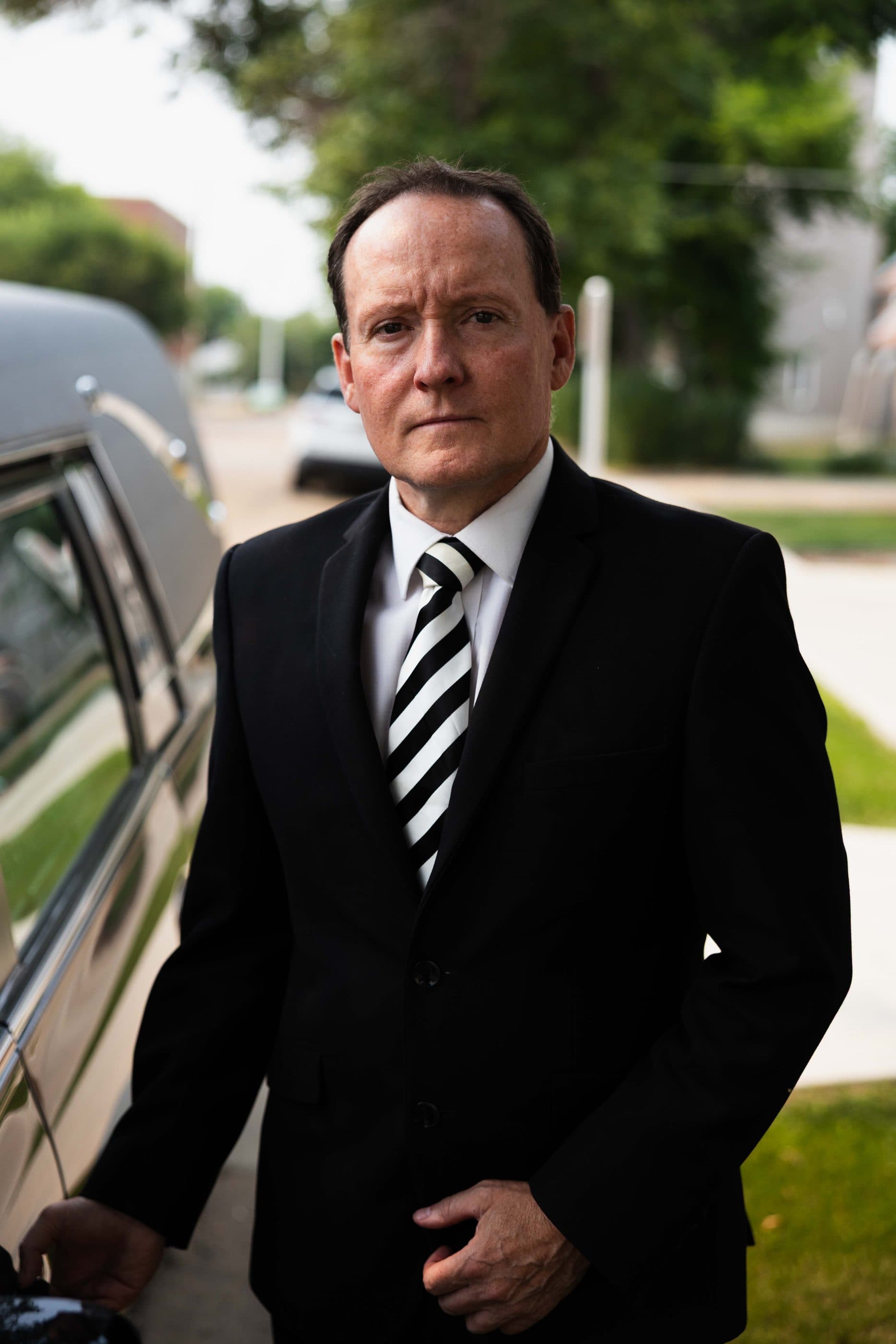 A funeral director waiting beside the hearse