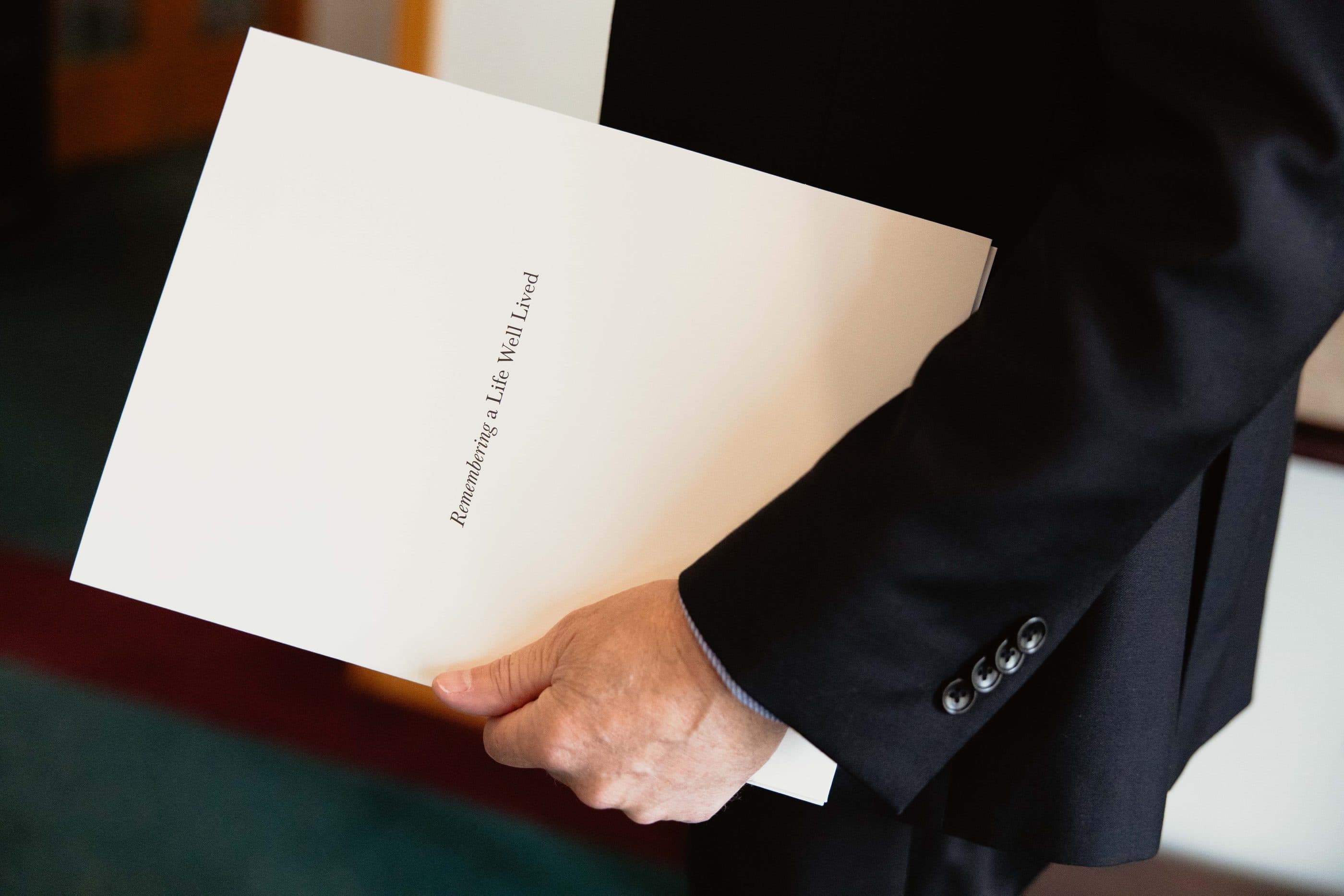 A funeral director holding a 'Remembering a Life Well Lived' planning folder