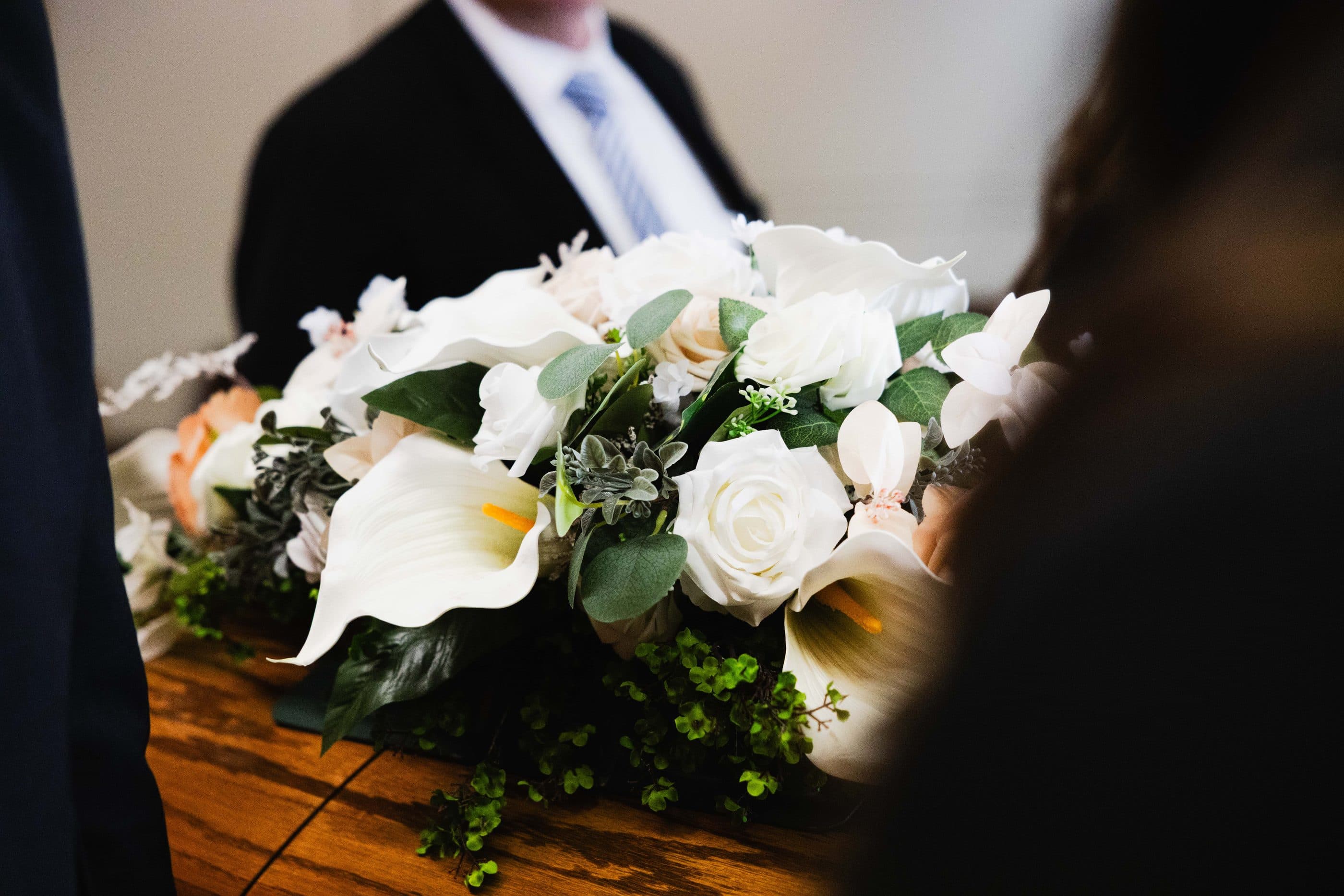 A spray of white roses and calla lilies resting on a casket