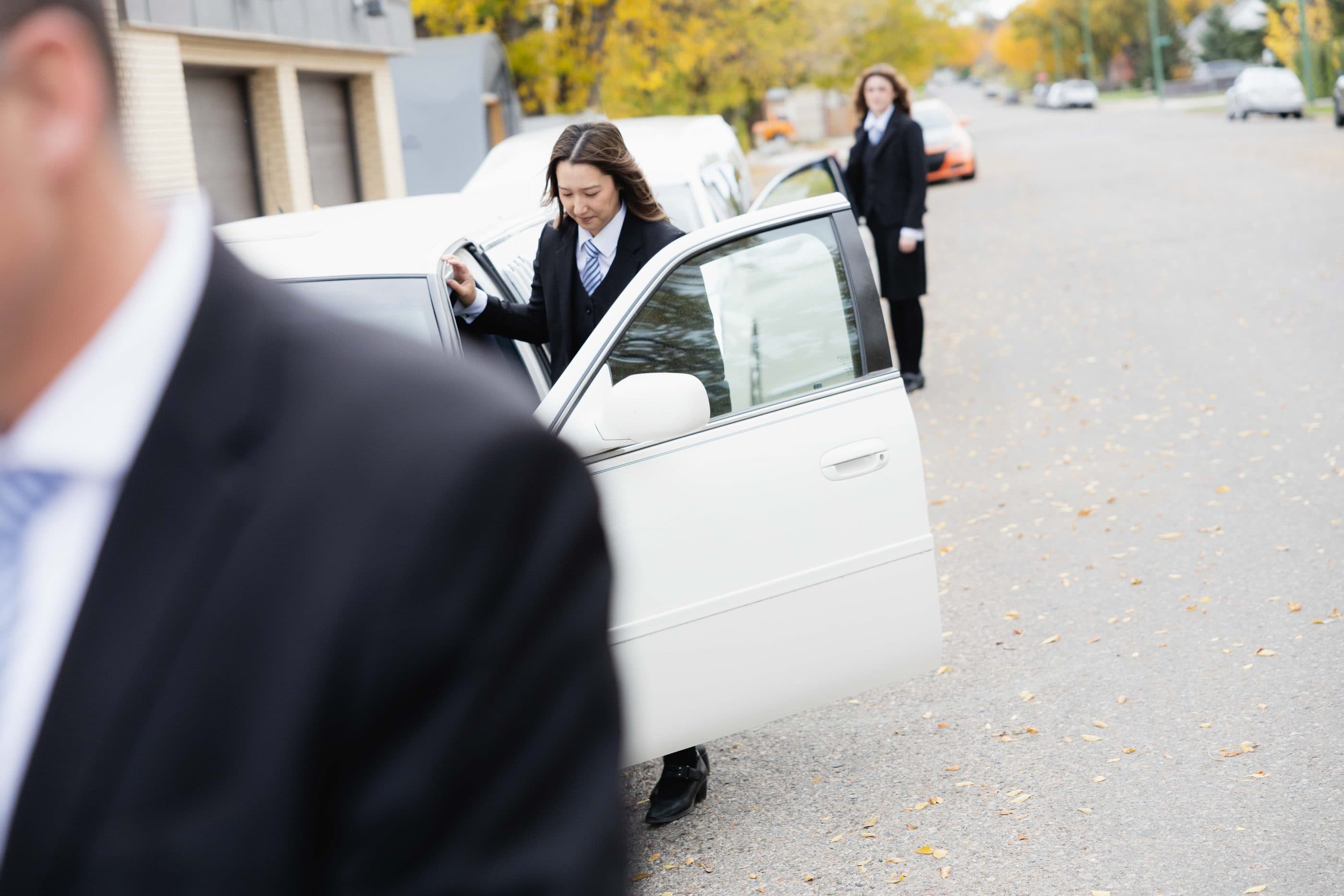 A director holding the car door open for a family on a quiet street