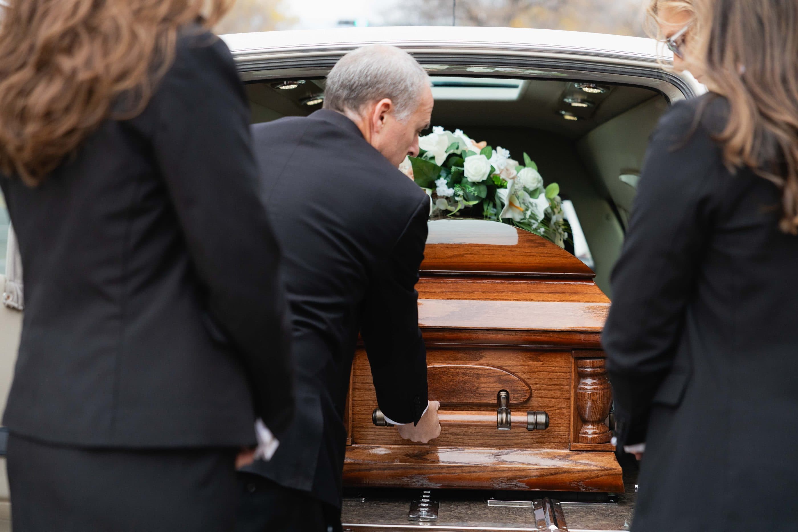 Funeral directors easing a casket into the hearse