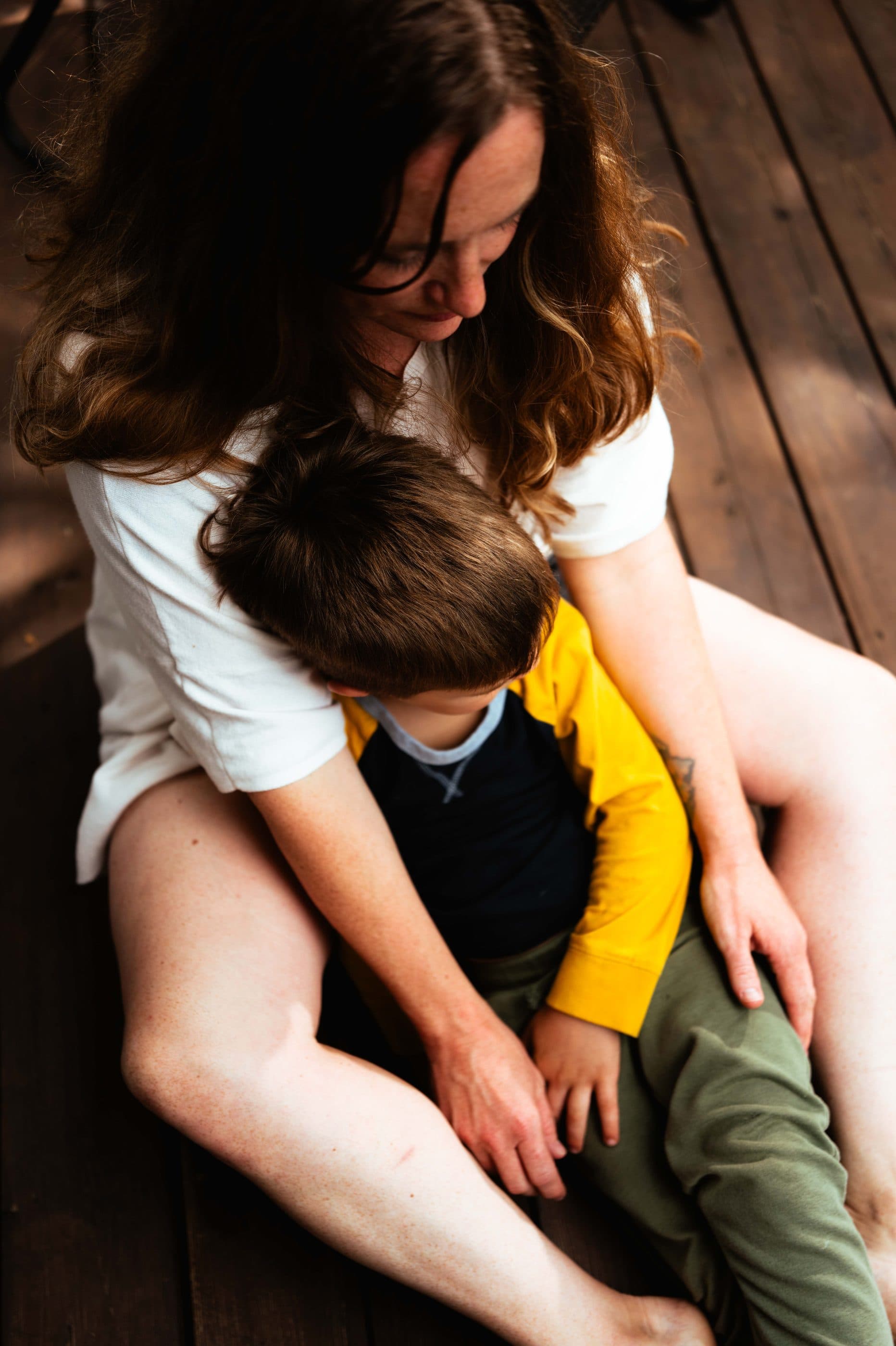 A mother sitting on a wooden deck with her young son in her lap