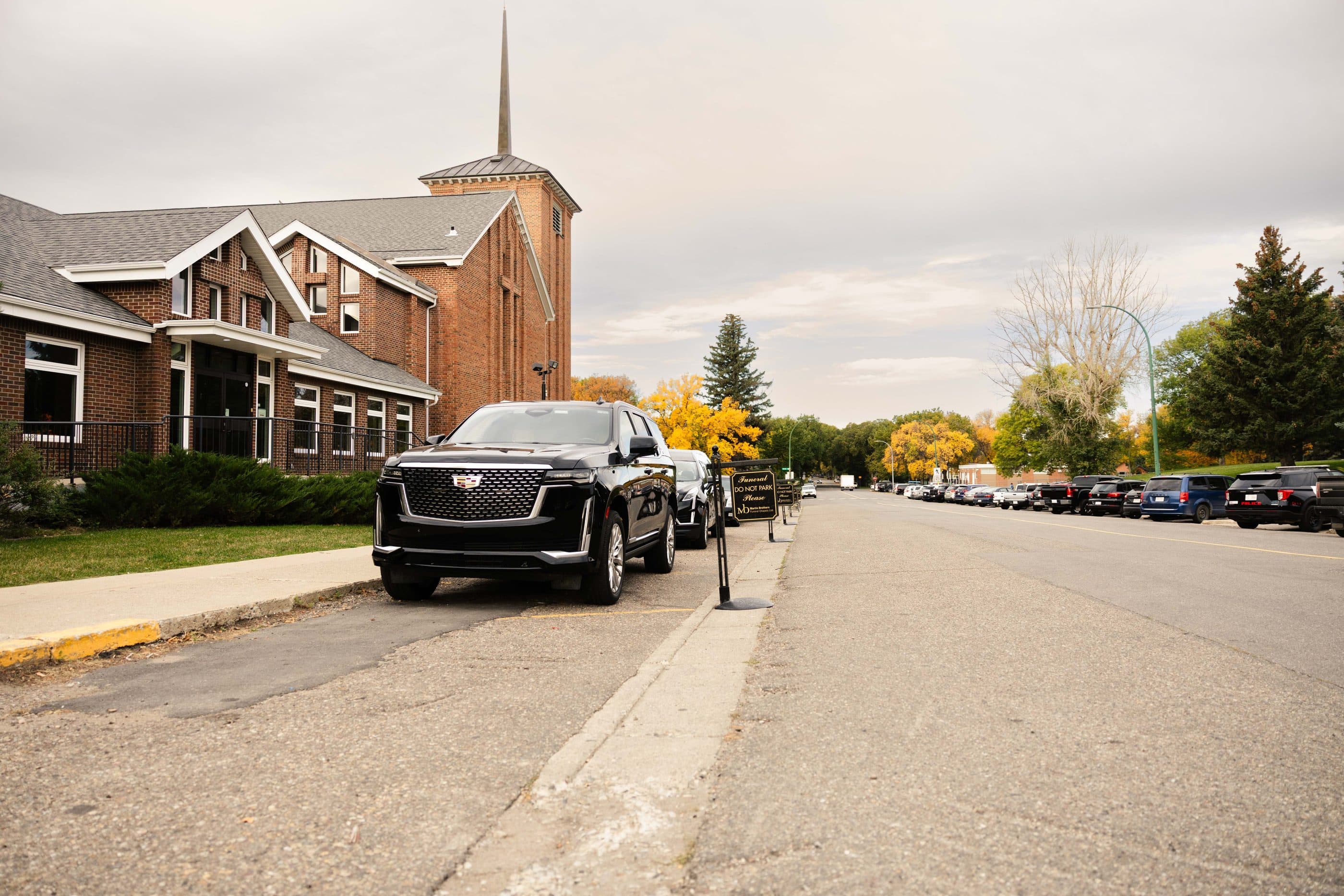 The cortege waiting outside the church on an autumn street, cars lining the road