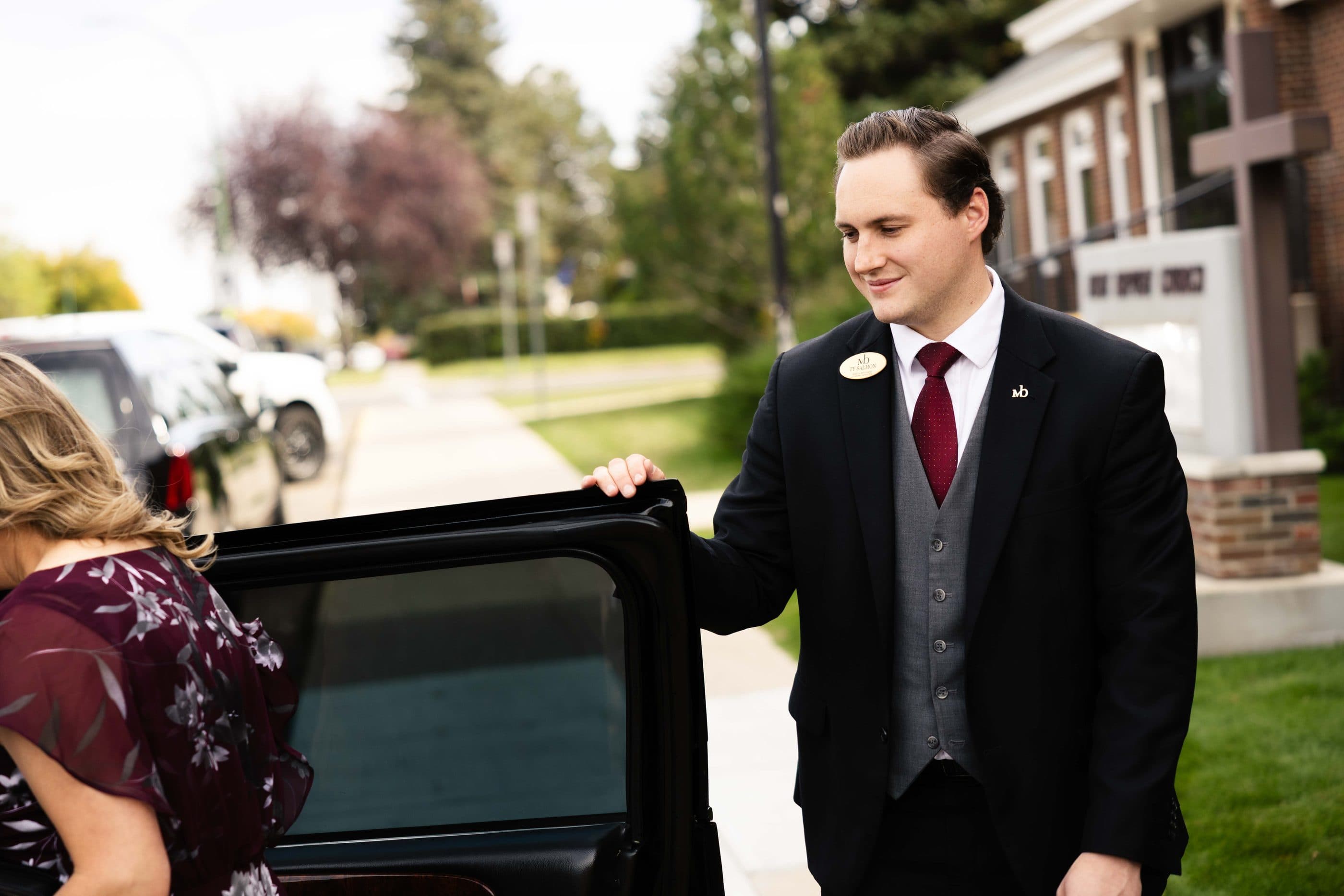 A funeral director holding the car door open for a family outside the church