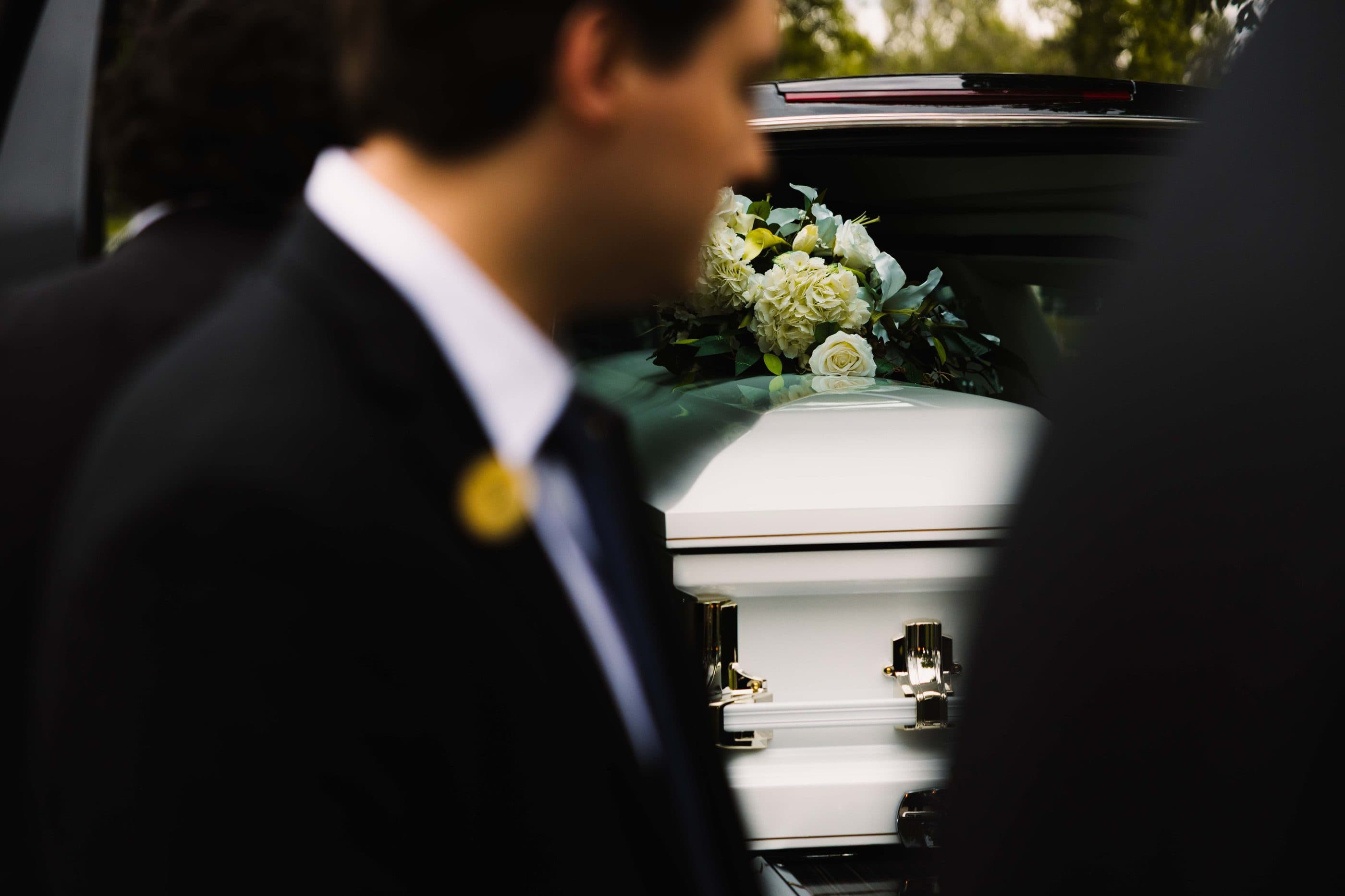 Pallbearers carrying a white casket dressed with roses