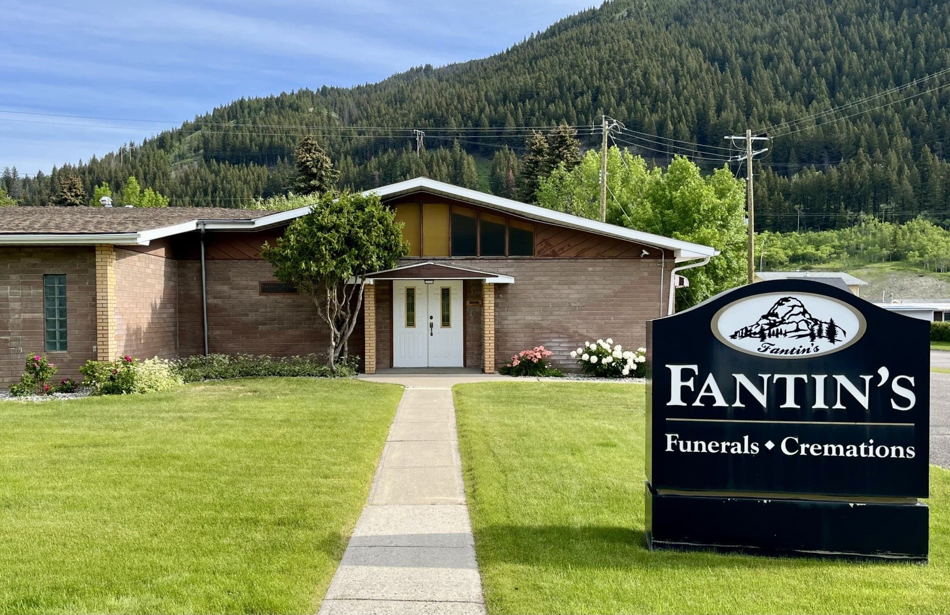 Fantin's Funeral Chapel in Blairmore, its sign out front and a forested slope of the Crowsnest Pass behind