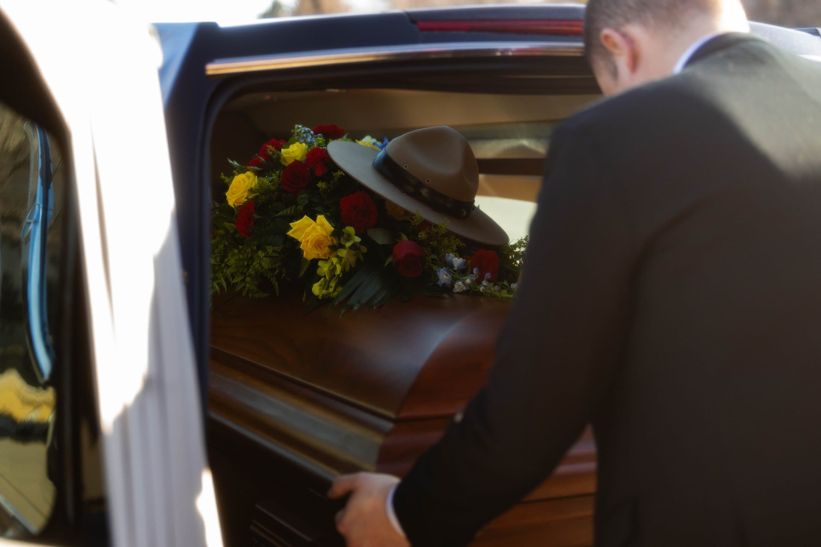 A funeral director placing flowers beside a casket in the hearse
