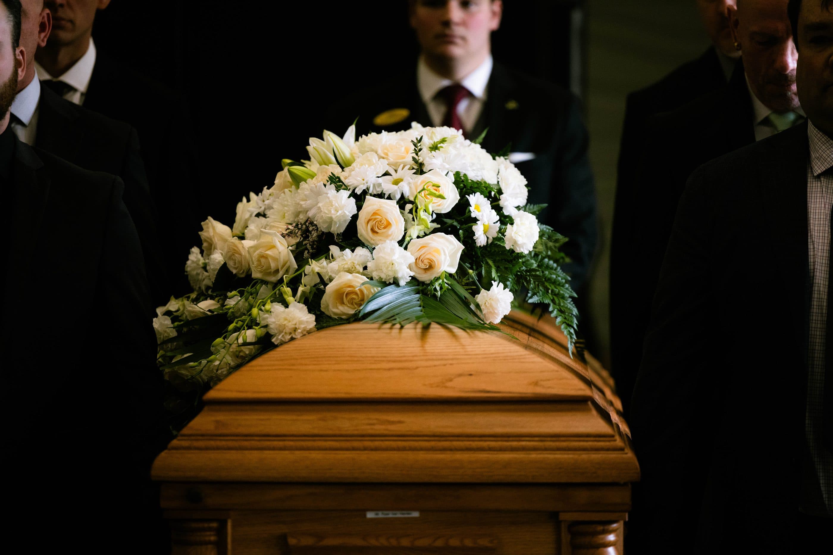 A casket dressed with white roses, carried by pallbearers