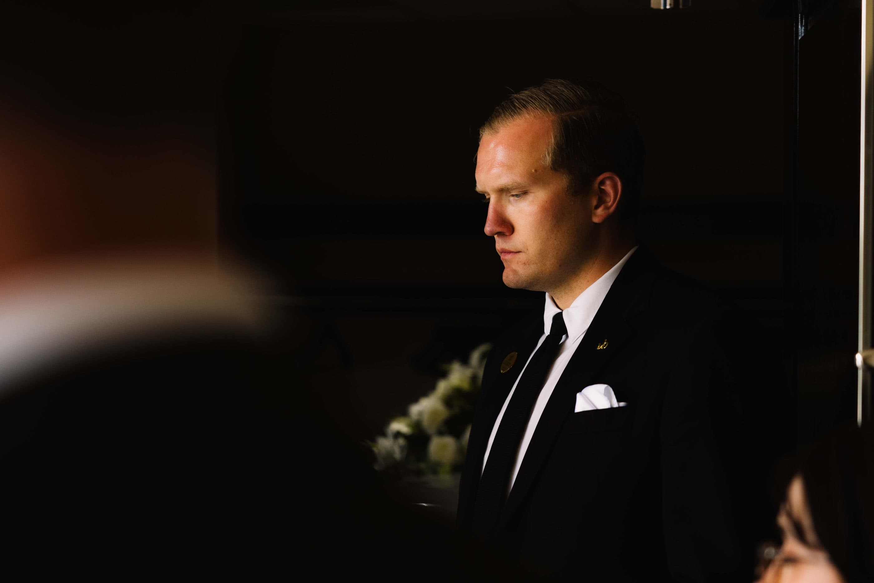 A funeral director in a dark suit, waiting quietly beside the chapel