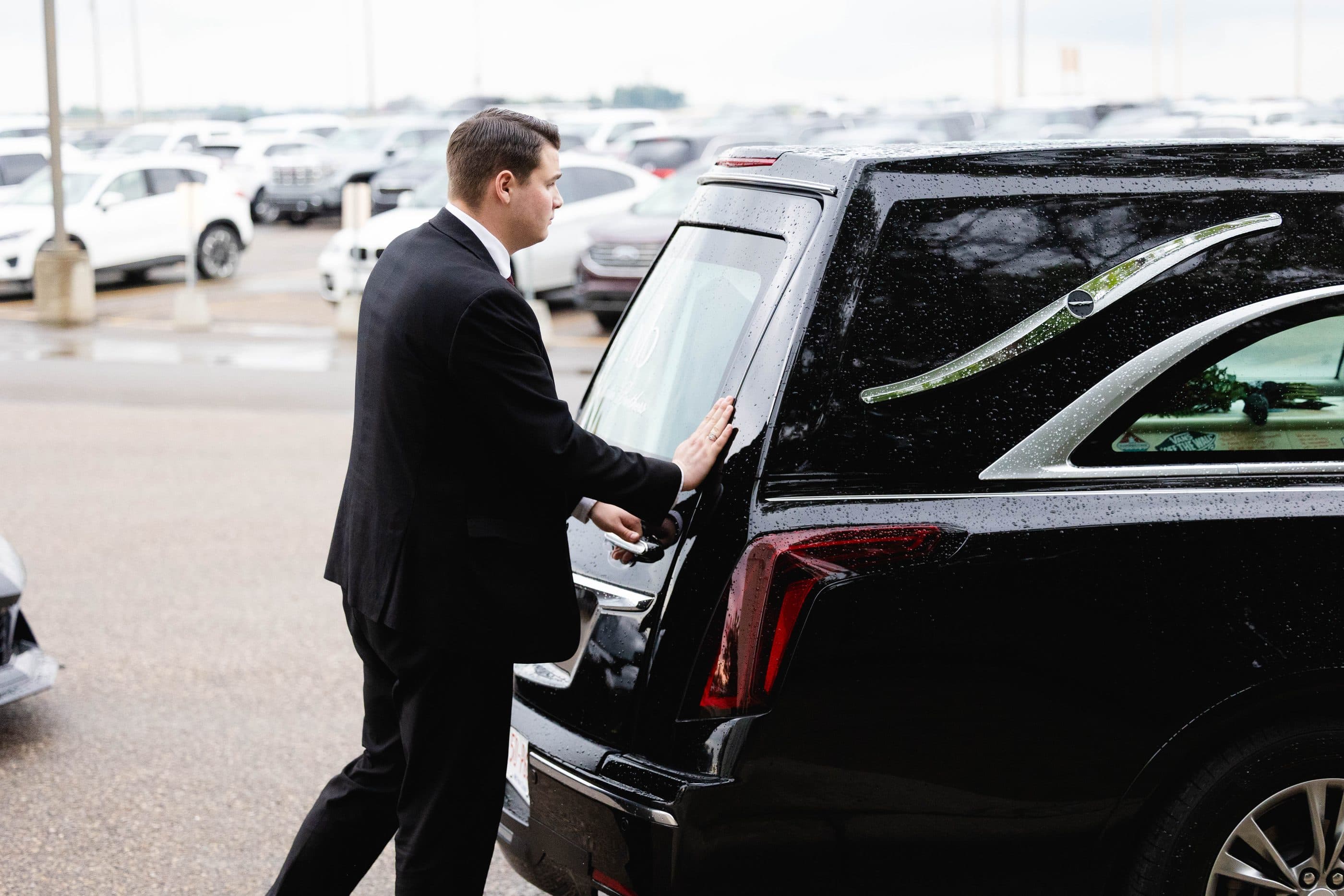 A funeral director opening the rear door of a hearse outside the chapel
